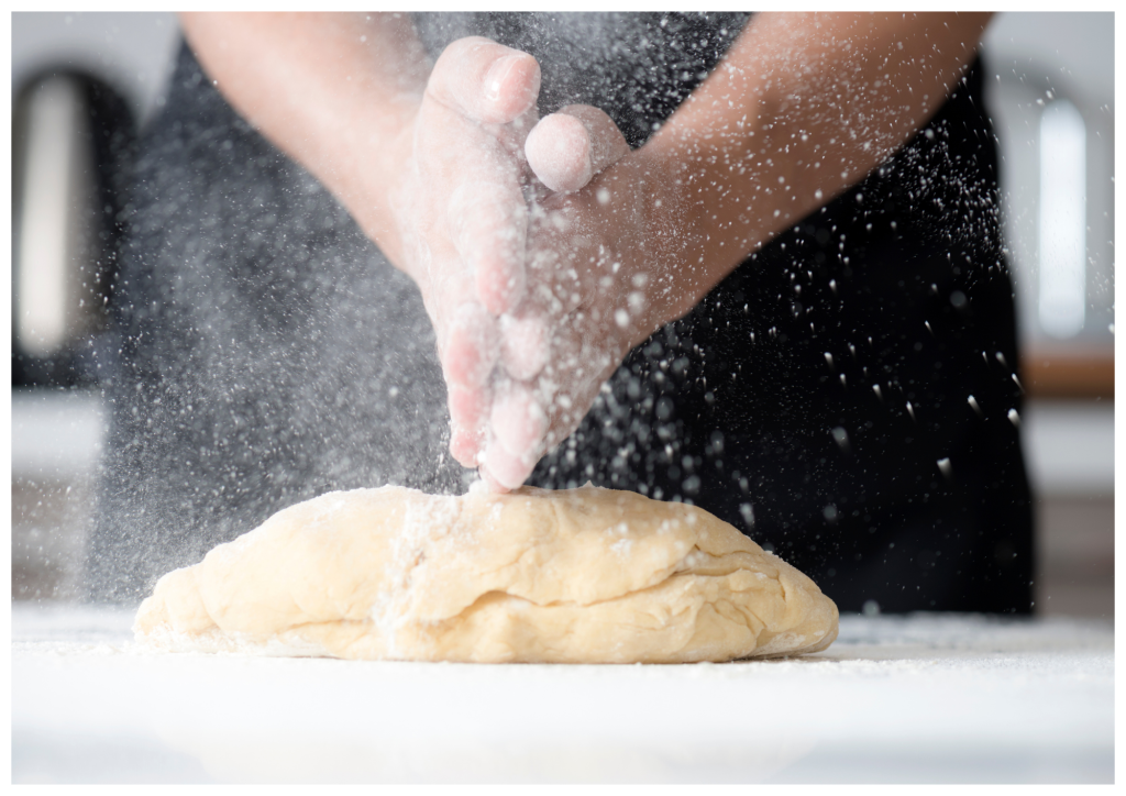 handen in het meel terwijl er een grote bol deeg wordt gekneed voor een biologisch brood